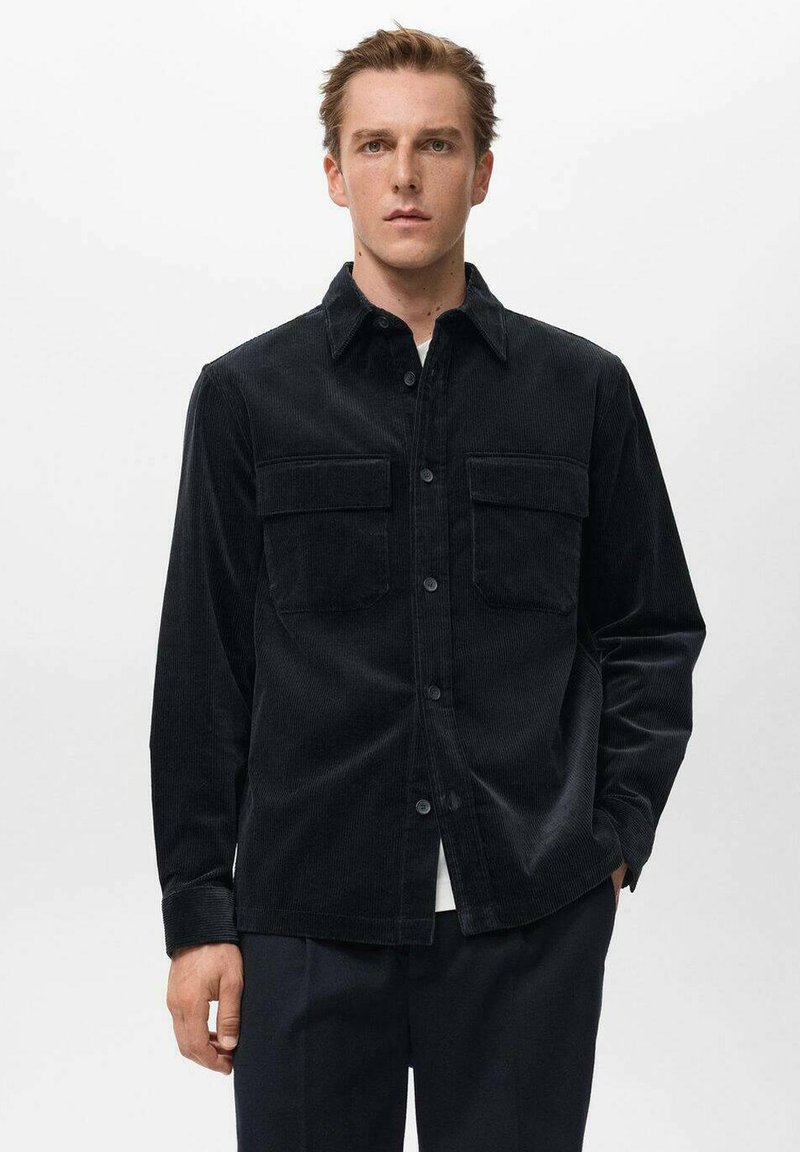 Camicia in corduroy nera con due tasche frontali applicate, design con bottoni, maniche lunghe e colletto, caratterizzata da una finitura ribattuta texturizzata.