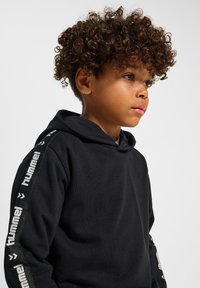 Schwarzer Kapuzenpullover mit einer Fronttasche und Logodetails entlang beider Ärmel. Hergestellt aus einem weichen Material; verfügt über eine Kapuze mit Kordelzug.
