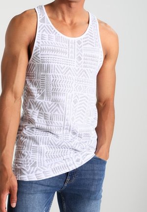 Débardeur blanc avec un motif géométrique en gris clair. Fabriqué en matériau léger avec un ourlet arrondi. Assorti à un jean bleu.