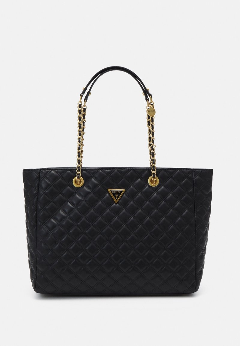 Sac fourre-tout noir matelassé avec quincaillerie dorée et doubles anses en chaîne. Il présente un accent de logo triangulaire sur le devant. Texture lisse.