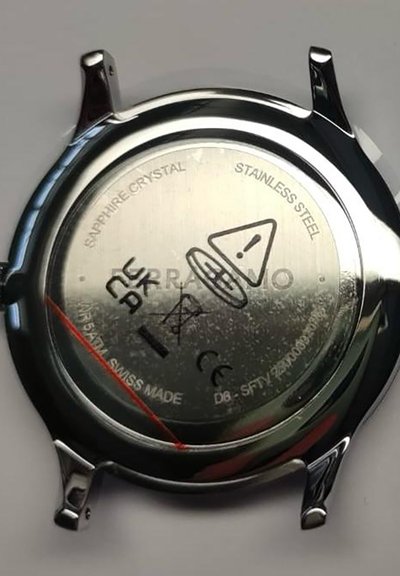 Back of a stainless steel watch case showing markings including "Sapphire Crystal," "Swiss Made," a warning symbol, and certification logos.