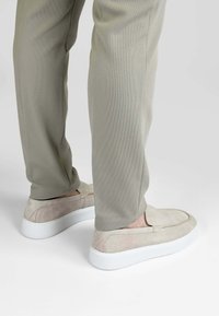 Beige instap schoenen met een suède bovenwerk en een witte rubberen zool. De schoenen hebben een minimalistisch ontwerp en een gladde afwerking.