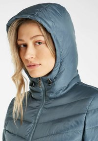 Leichte, isolierte Jacke in Schieferblau mit durchgehendem Reißverschluss, hohem Kragen und verstellbarer Kapuze. Merkmale sind horizontale Nähte.