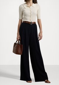 Krémový žebrovaný pletený kardigan s krátkými rukávy, zkombinovaný s černými širokými kalhotami, hnědým opaskem a texturovanou hnědou kabelkou.