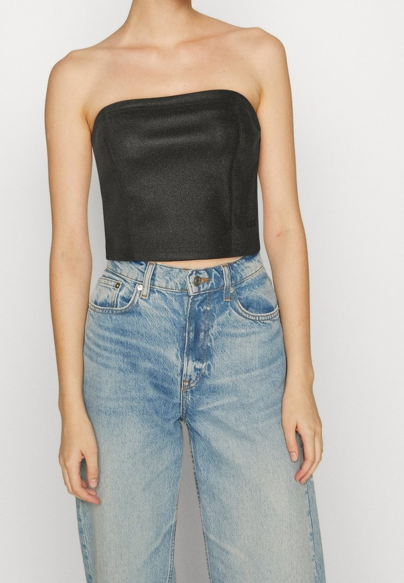 Haut noir court sans bretelles en tissu lisse, associé à un jean taille haute bleu clair avec un effet délavé et un design classique à cinq poches.
