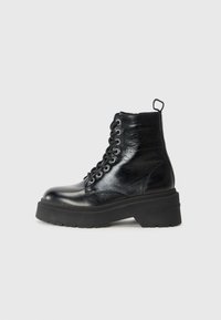 Bottines noires à finition brillante, dotées d'une semelle épaisse et d'un design à lacets, affichant fièrement la marque "TOMMY."