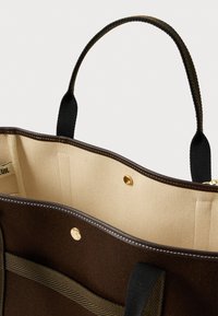 Καφέ τσάντα ώμου με μπεζ υφασμάτινη εσωτερική επένδυση, μαύρους χειρολισθήρες και χρυσά κουμπιά, απεικονιζόμενη από πάνω.