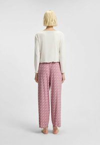 Wit kort cropped langmouwtop met gerimpelde randen, gedragen met een roze pyjamabroek met een witte, verspreide print en gerimpelde zomen.