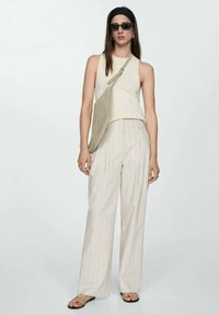 Débardeur à côtes beige clair associé à un pantalon large à rayures claires. Les accessoires comprennent un sac bandoulière vert et des lunettes de soleil noires.