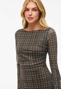 Robe à manches longues avec un motif à carreaux sombre. Présente un corsage ajusté avec des détails froncés et un col bateau. Fabriquée en tissu léger.