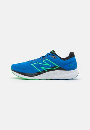 Zapatillas deportivas azules con acentos negros y detalles verdes. Cuentan con una parte superior de malla transpirable, una suela acolchada y un logotipo visible.