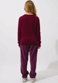 Stickad vinröd tröja med avslappnad passform, ribbade ärmslut och midja, matchad med ribbade vinröda byxor och neutrala sneakers.