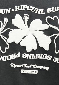 Λευκά άνθη ιβίσκου και κείμενο λογοτύπου Ripcurl Surf Company σε μαύρο ύφασμα, με το «Since 1969» κάτω από το σχέδιο.