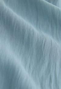 Gaiši zila auduma ar gludu tekstūru, kuram ir smalkas vertikālas svītras. Materiāls izskatās mīksts un nedaudz atreflectējošs.