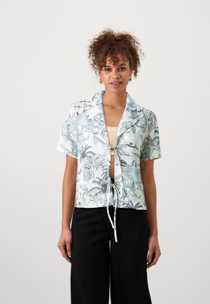 Short-sleeved shirt in light blue fabric with a botanical print, featuring a tie-front design and collar. Paired with black wide-leg pants.
