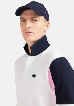 Polo blanc avec manches courtes bleu marine et rose, col bleu marine et patte de boutonnage. Comprend un logo sur la poitrine.