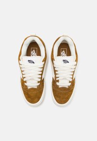 Brune semskede sneakers med hvite snører og en hvit gummi såle. Har et logomerke på tungen og myk fôr rundt ankelen.