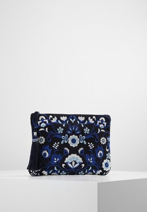 Zwarte stoffen clutch met blauw en wit bloemrijk borduurwerk en een donkerblauwe kwast bevestigd aan de rits, tentoongesteld op een wit oppervlak.