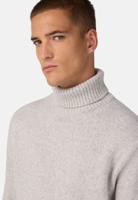 Hellgrauer Rollkragenpullover mit geripptem Kragen und strukturiertem Strickmuster, der eine lockere Passform und minimale Details aufweist.