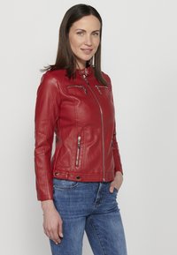 Red leather jacket with zippered pockets, standing collar, and fitted design. Worn over blue denim jeans. Smooth texture.