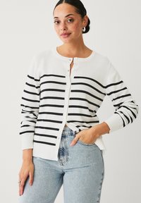 Cardigan bianco con strisce orizzontali nere, scollatura rotonda, chiusura con bottoni e polsini a costine. Design leggero e aderente.