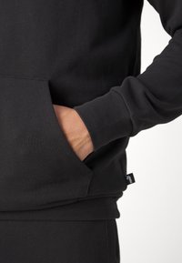 Felpa nera realizzata in misto cotone, con tasca frontale, polsini a costine e una piccola etichetta del brand sull'orlo. Texture morbida.