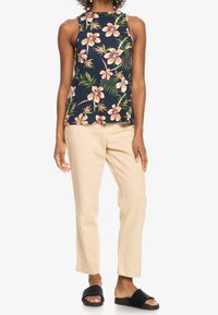 Mörkblå blommig linne med rosa blommor, kombinerad med ljusbeiga byxor. Modellen har på sig svarta sandaletter.