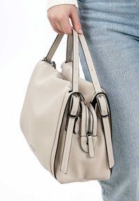 Beige leather handbag with a textured surface, two handles, a zippered pocket, and silver hardware accents. Compact design with rounded shape.