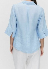 Himmelblaues Leinenbluse mit Kragen, Dreiviertelärmeln mit Schlitzen und Knopfdetails sowie einem abgerundeten Saum hinten.