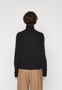 Schwarzer Rollkragenpullover mit langen Ärmeln, aus einem weichen Strickmaterial. Verfügt über eine lockere Passform und einen gerippten Kragen für zusätzliche Textur.