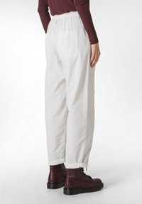 Pantaloni bianchi, larghi e comodi, con vita elastica e due tasche posteriori, abbinati a stivali alla caviglia bordeaux. Tessuto liscio, leggermente strutturato.