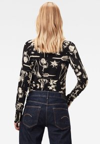 Langærmet sort top med cremede blomster mønster, parret med mørke denim jeans med stikninger på baglommerne og en glat talje.