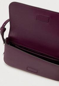 Bolsa de ombro roxa em couro, com o interior liso visível e alça ajustável com detalhe de fivela.