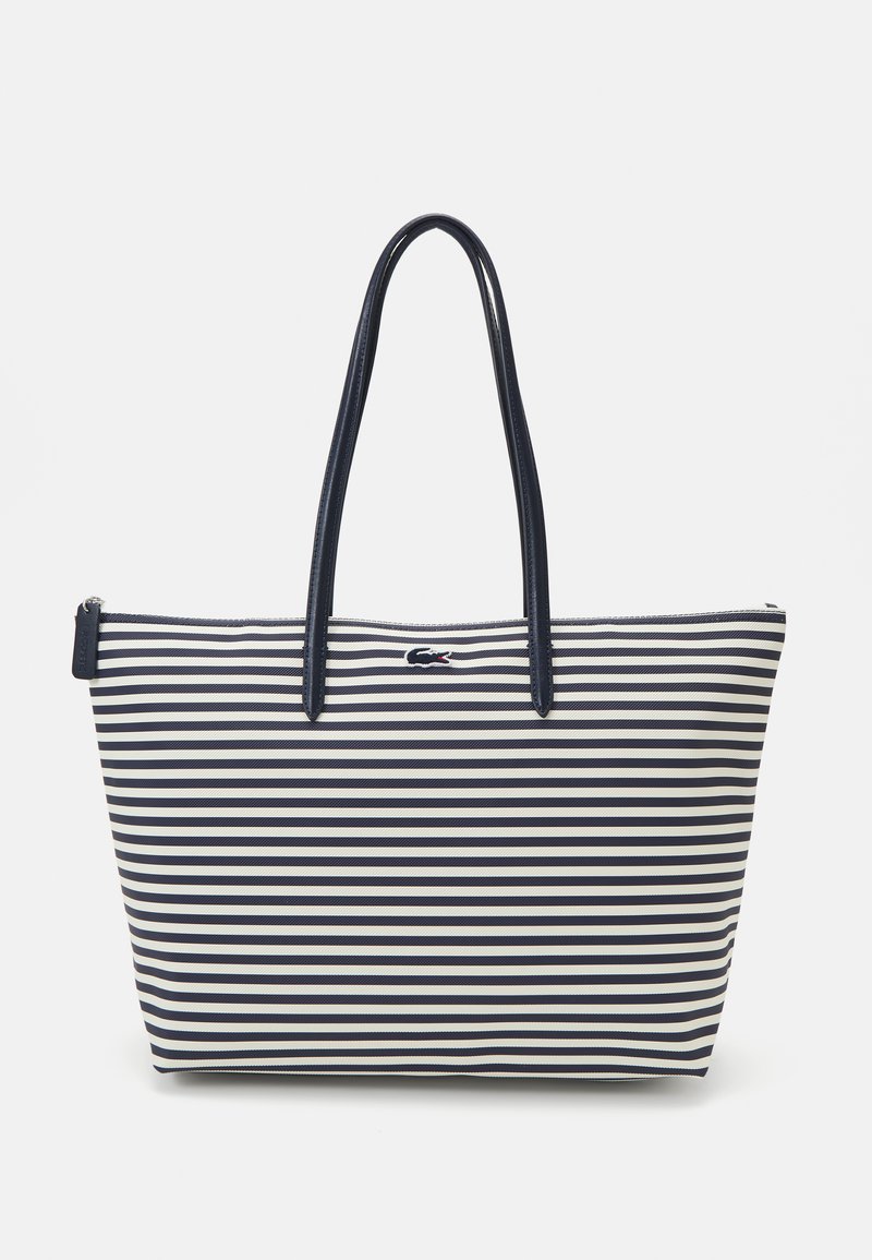 Sac fourre-tout rayé avec des rayures verticales bleu marine et blanches, en tissu lisse, avec deux longues poignées, fermeture éclair, et un petit logo en accent.