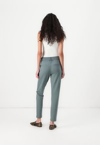 Lys grønne bukser med elastisk liv, taperet pasform og baglommer, parret med sorte og beige leopardprint slip-on sko.