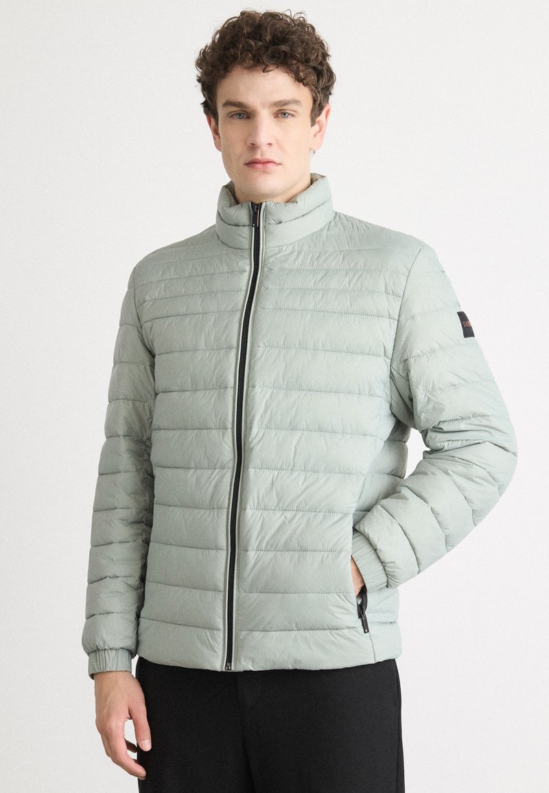 Light green puffer jacket with horizontal quilted design, high collar, front zipper, and elastic cuffs. Features side pockets and black accents.
