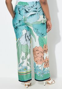 Un pantalon large en tissu léger à fleurs présente de grandes fleurs bleues et pêches, des feuilles vertes et un ourlet à motifs avec des rayures et des accents.
