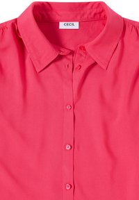 Chemise rose vif à boutons avec col pointu et étiquette de marque visible "Cecil" à l'intérieur du col.
