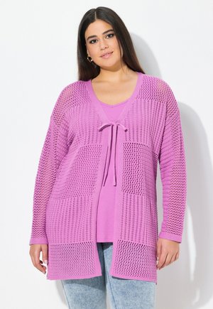 Cardigan lavorato a maglia rosa con un motivo testurizzato, caratterizzato da sezioni a trama aperta e una chiusura a cravatta nella zona del collo, indossato sopra un top abbinato.