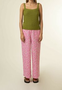 Olivgrön stickad linne med tjocka spännen, parat med löst sittande rosa byxor med blommönster. Platta sandaler med dekorativa detaljer.