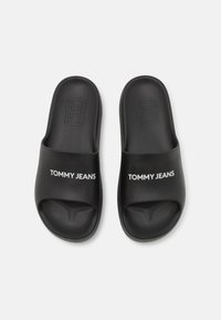 Černé skluzavkové sandály s texturovaným popruhem a bílým logem "TOMMY JEANS". Vyrobené z odolného syntetického materiálu, design s jednoduchým nazouváním.