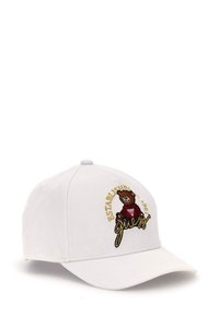 Cappellino da baseball bianco con visiera curva, caratterizzato da un logo di orso ricamato in testo marrone e oro che legge "FONDATO NEL 1981 Guess."
