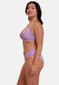 Reggiseno in pizzo lilla con slip coordinati. Il reggiseno presenta coppe in pizzo floreale, spalline regolabili e bordi scollati. Gli slip hanno dettagli in pizzo e tessuto liscio.