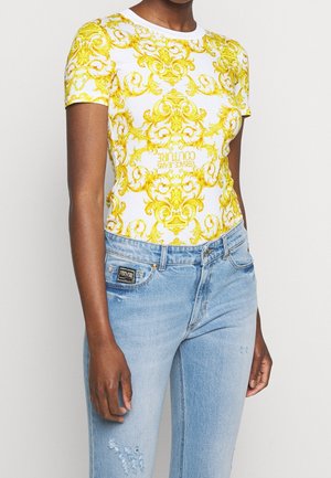 Strak gesneden wit overhemd met korte mouwen en ingewikkelde gele barokpatronen, gecombineerd met lichtblauwe distressed jeans met een merkpasje.