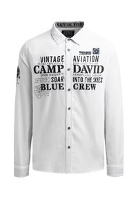 Weißes Hemd mit Button-Down-Kragen, das schwarzen Drucktext und Logos, blaue Knöpfe und lange Ärmel mit kontrastierenden Nähten aufweist.