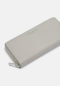 Portefeuille zippé en cuir gris clair avec une texture lisse. Présente un logo embossé, des coutures contrastées et des accessoires en métal argenté.