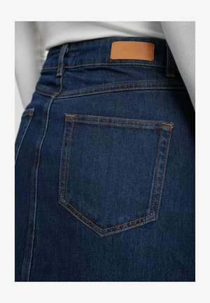 Denimrock in tiefblau mit orangefarbenen Nähten. Verfügt über eine Gesäßtasche und ein braunes Lederetikett am Bund.