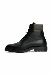 Schwarze Leder-Schnürstiefel in Knöchelhöhe mit gepolstertem, dunkelgrauem Kragen und dicker Sohle, die nahe der Ferse in Rot, Weiß und Blau gestaltet ist.