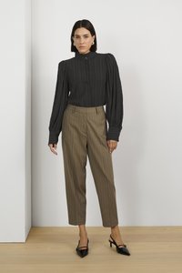 Blusa nera a righe con maniche a sbuffo, abbinata a pantaloni marroni a righe. Tacchi neri con punta a forma di freccia completano l'outfit.