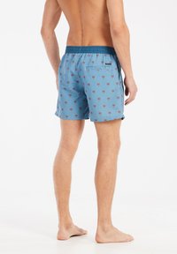 Mėlynos maudymosi šortai su palmių raštu, elastinga juosta ir užpakaliniu kišeniu. Lengvas audinys, vidutinio ilgio iki šlaunikaulio ir tekstūruota apdaila.